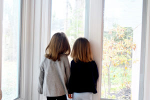 Two young girls looking out a window at the trees.