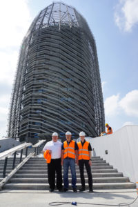 Three men in safety vests standing next to a tall building.