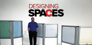 A man standing in front of a wall with the words " designing spaces ".